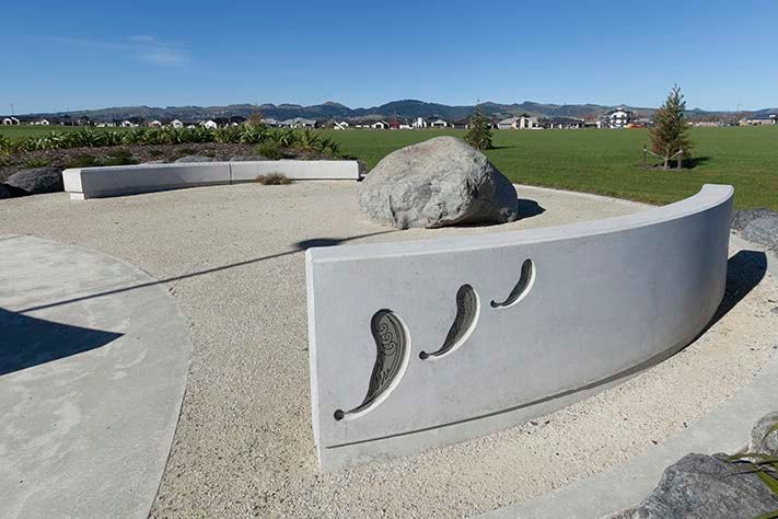 A cultural landmark sits of stone and concrete sits on a green landscape with medium density developments in the background.