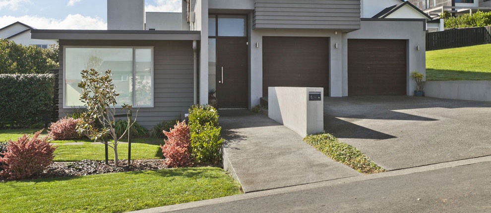 Two seperated garages attached to one house with a green lawn with small bushes and trees