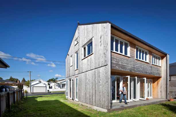 The zero energy house,  positioned on the site to maximise its potential , a man is stnading outside on the deck in the sun