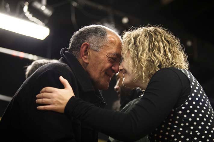 A māori man and pakeha woman come together in a customary greeting.