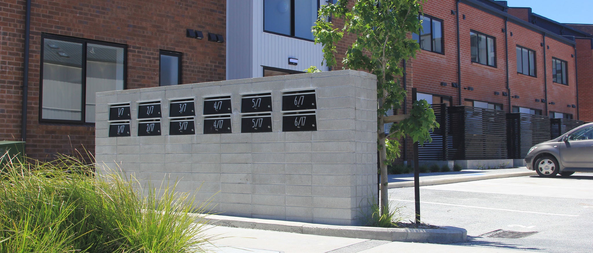 The photo shows 2 rows of 6 black letter boxes in a concrete wall with red brick terraces in the background.