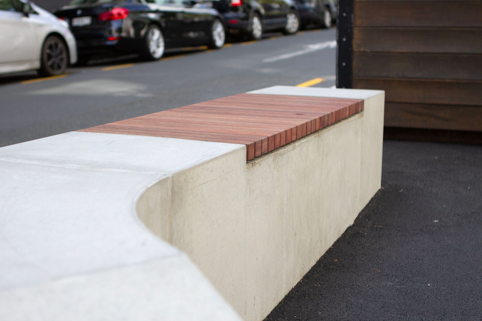 Looking close up at the wooden slats inset in a concrete bench at Paul's street in downtown Auckland. The background is a blurry streetscape.