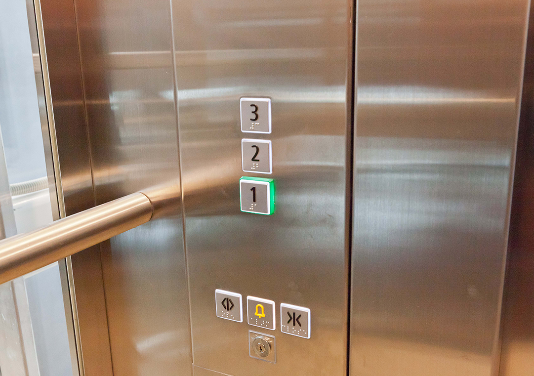 This lift has buttons with raised tactile numbers and Braille placed at a height which allows them to be pushed by all users. The emergency buttons are clearly demarcated through colour contrast. The selected floor is lit. Better practice is to locate Braille to the side of the buttons to enable them to be read without being accidentally pressed.