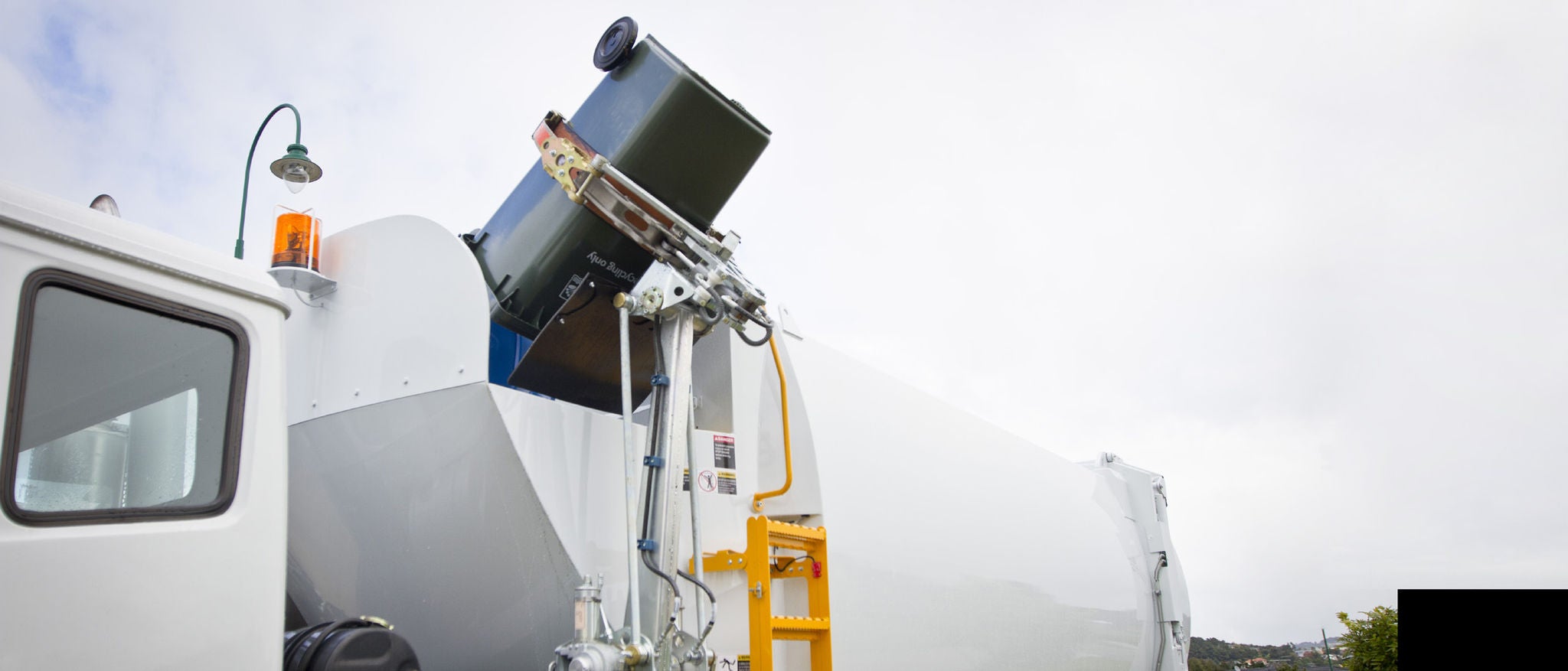 A white coloured rubbish bin is in the process of emptying the contents into the truck