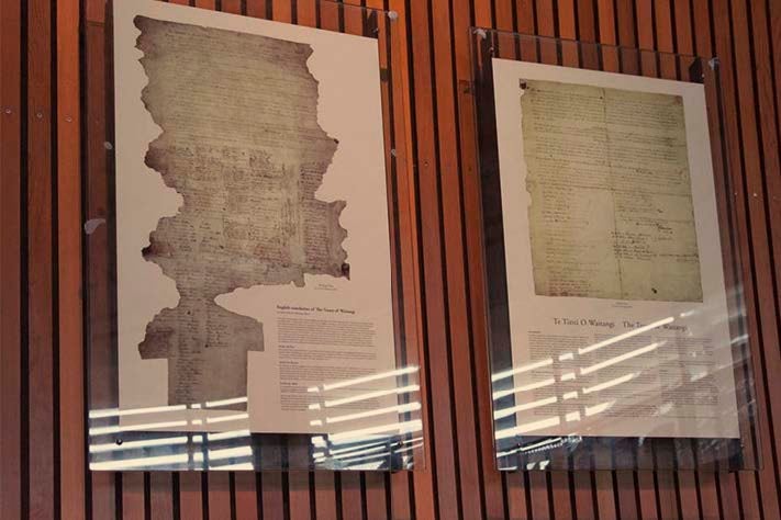 Copies of the Te Tiriti O Waitangi/The Treaty of Waitangi hang on the wall in a display in a glass case