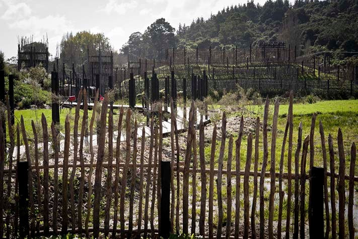 A pah site with palisades and whare before green shrouded hills.